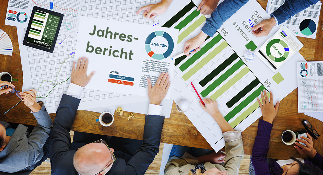 Bild Team am Besprechungstisch mit Diagrammen und einem Blatt „Jahresbericht“, von oben