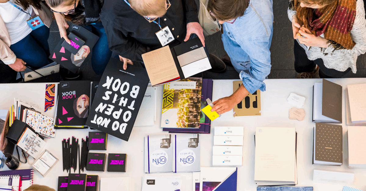 Bild Person sitzt mit aufgeschlagener Broschüre und einer Tasse Kaffee auf dem Sofa.