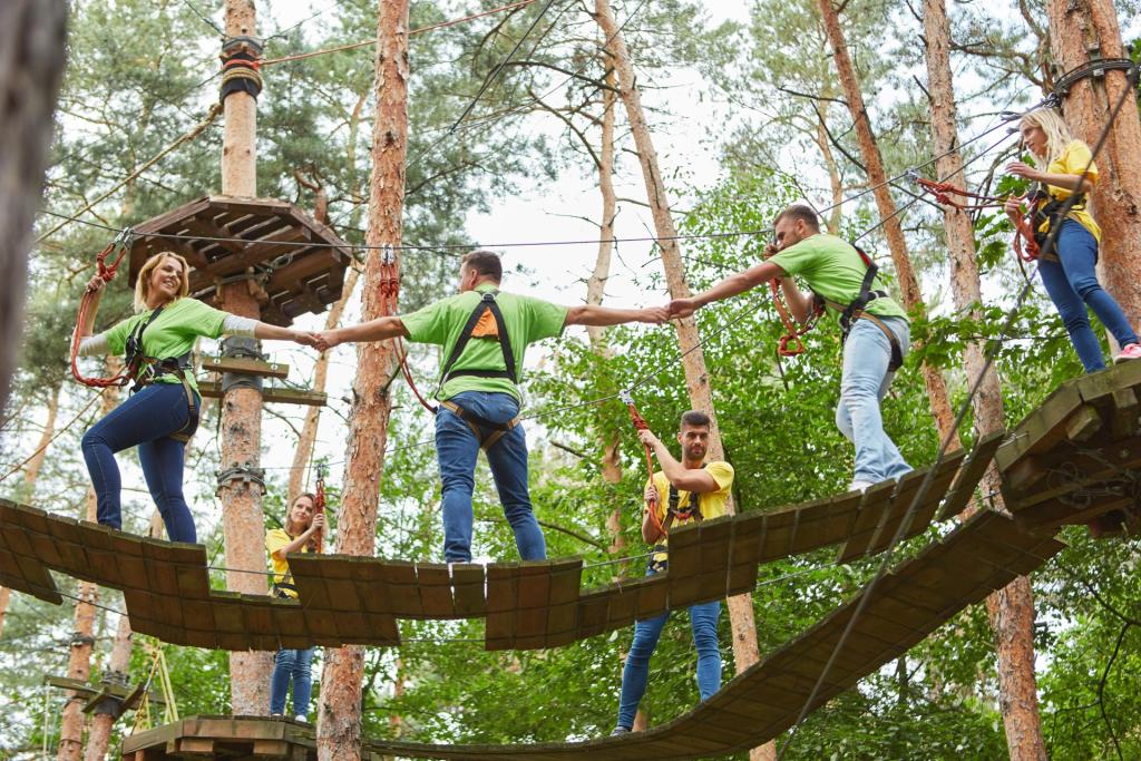 Teammitglieder halten sich gemeinsam auf einem Klettergarten an den Händen und überqueren eine schwingende Holzbrücke Teammitglieder halten sich gemeinsam auf einem Klettergarten an den Händen und überqueren eine schwingende Holzbrücke
